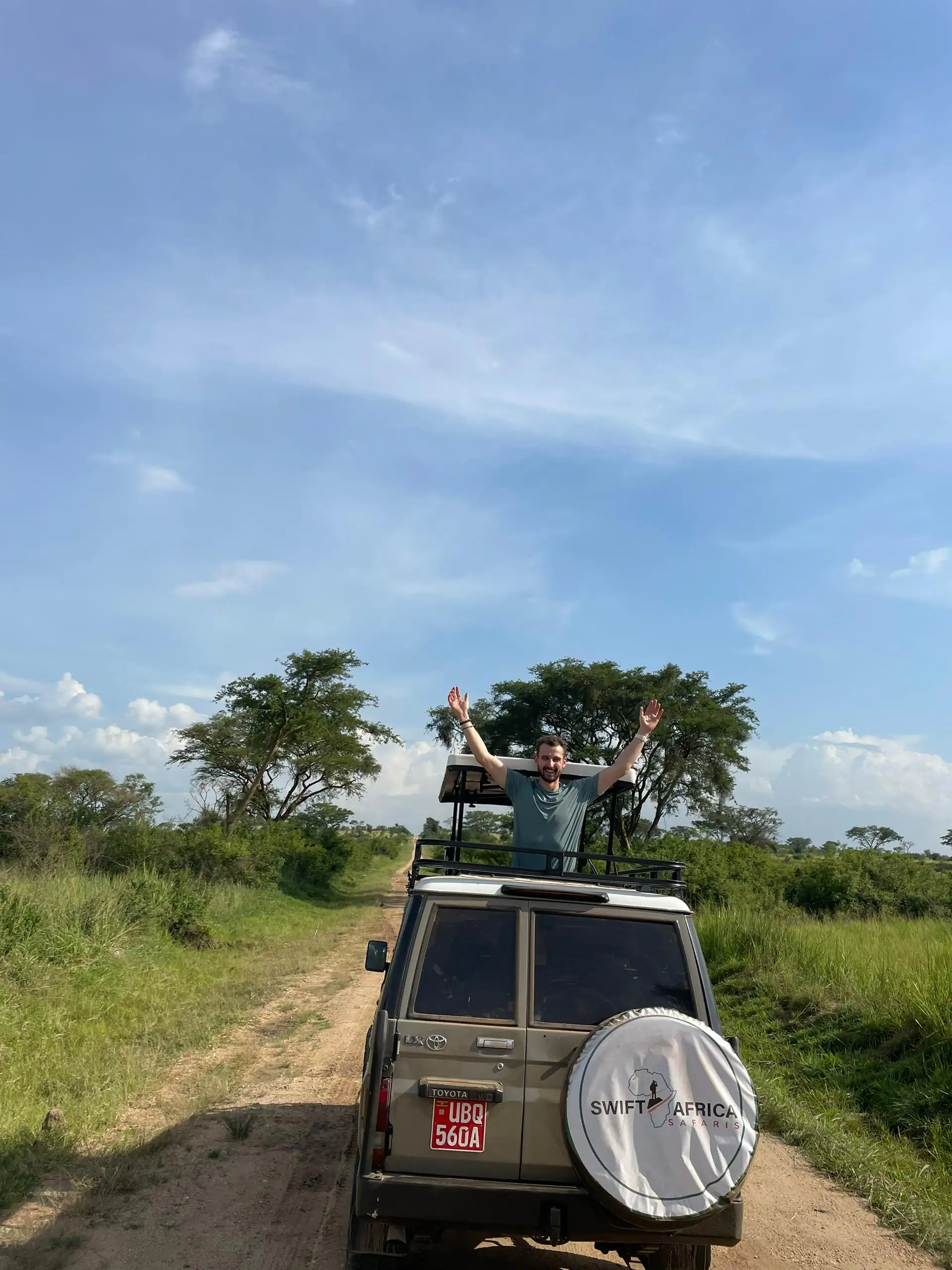 Happy traveler standing through the open rooftop of a branded safari vehicle in Uganda, arms outstretched while enjoying a wildlife safari adventure, illustrating the experience offered by a trusted Uganda tour operator and key factors to consider when choosing the best safari company.