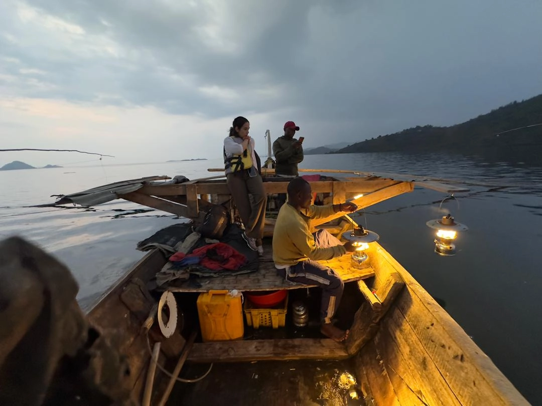 Local fishermen night fishing with a woman traveler in a traditional boat on Lake Kivu along the Congo Nile Trail, Rwanda — authentic cultural travel experience.