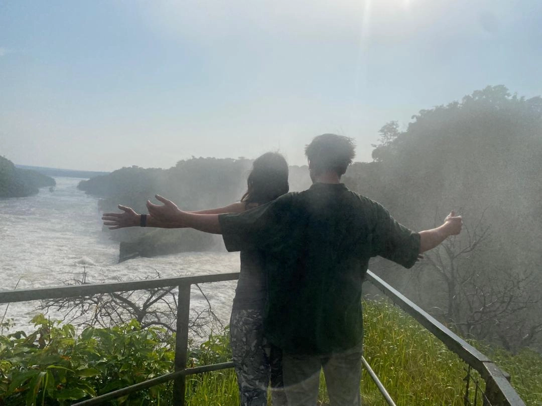 Couple standing with arms open overlooking Murchison Falls, comparing Queen Elizabeth vs Murchison Falls Safaris, romantic safari experience in Uganda.