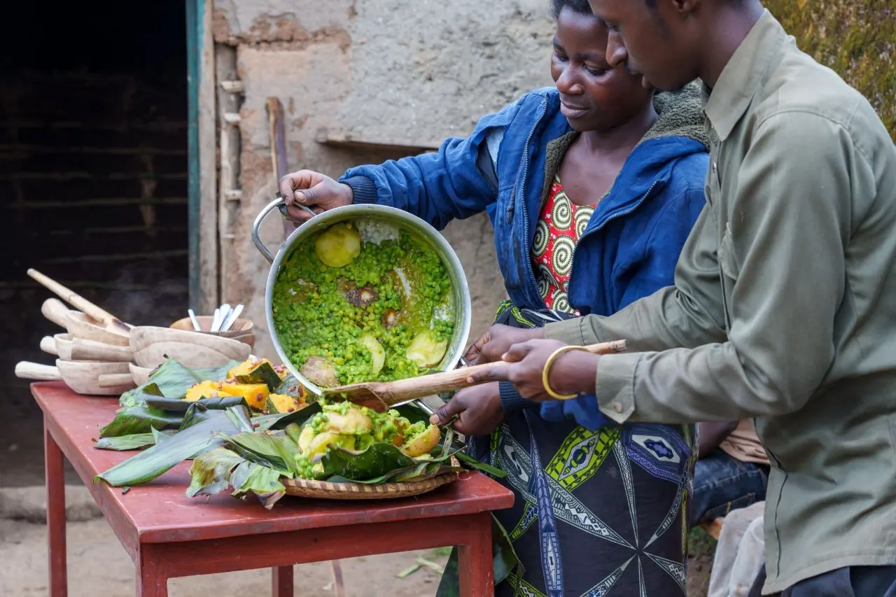 Local Rwandan villagers serving traditional food to international guests during an authentic cultural tour experience in Rwanda, showcasing community-based tourism, local cuisine, and cultural heritage.