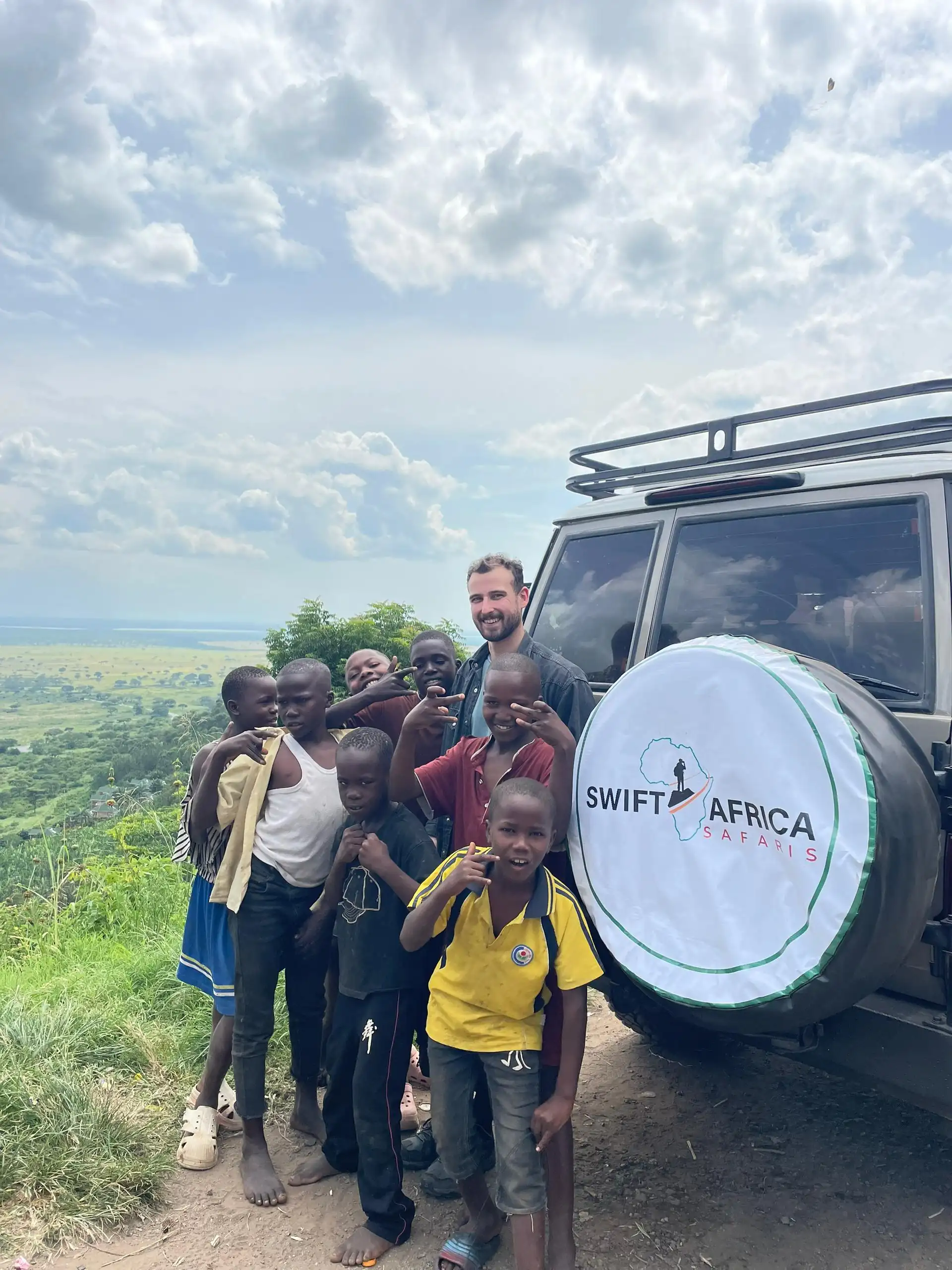 Family safari experience in Uganda with international guests and children standing beside a branded safari vehicle, showcasing a trusted Uganda tour operator and family-friendly wildlife adventure in East Africa.